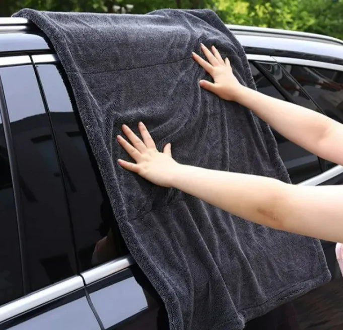 Person using a large gray towel to clean or dry a car